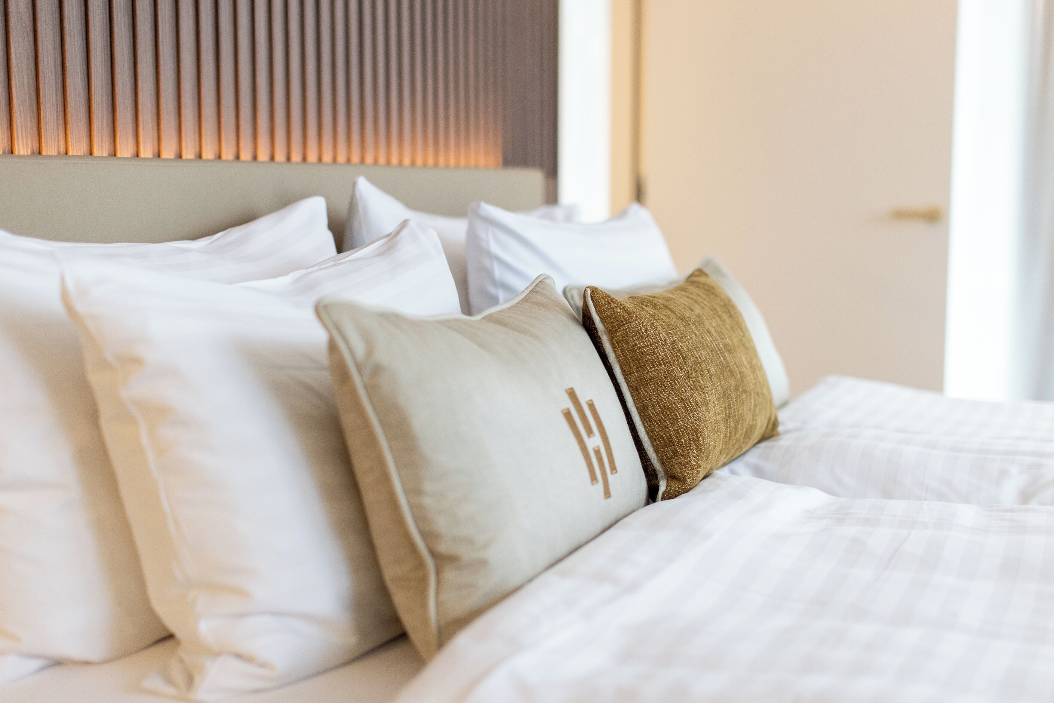 Ein ordentlich gemachtes Bett mit weißer Bettwäsche und mehreren Kissen, darunter ein auffälliges braunes Kissen.