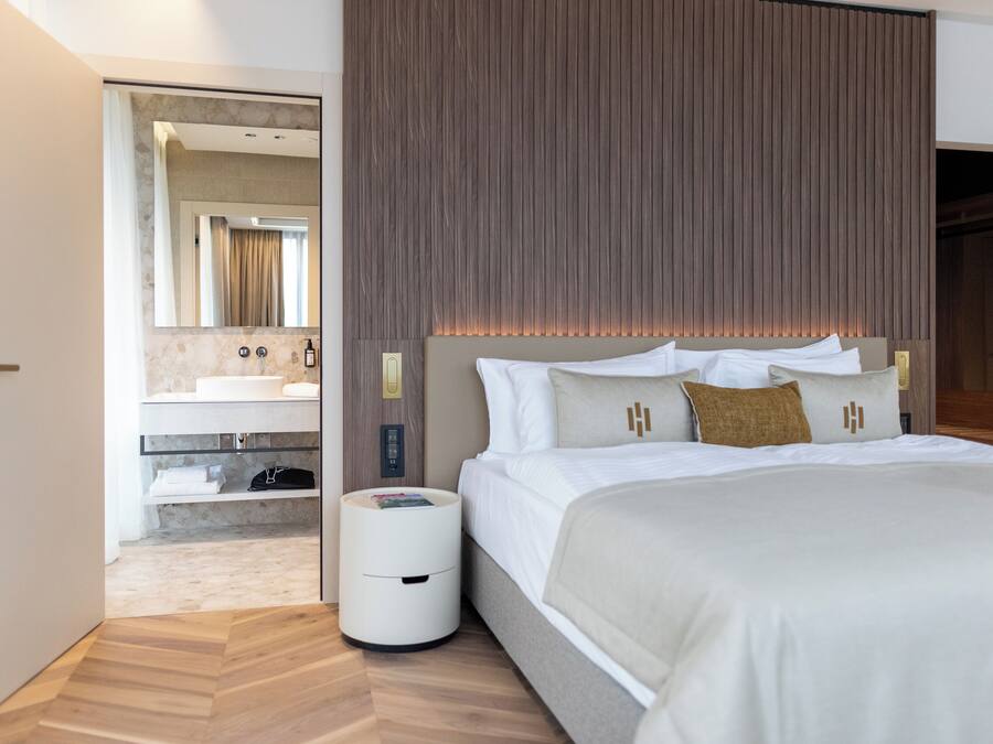 A modern hotel room with a large bed, a built-in vanity with a mirror, and a wooden panel wall.