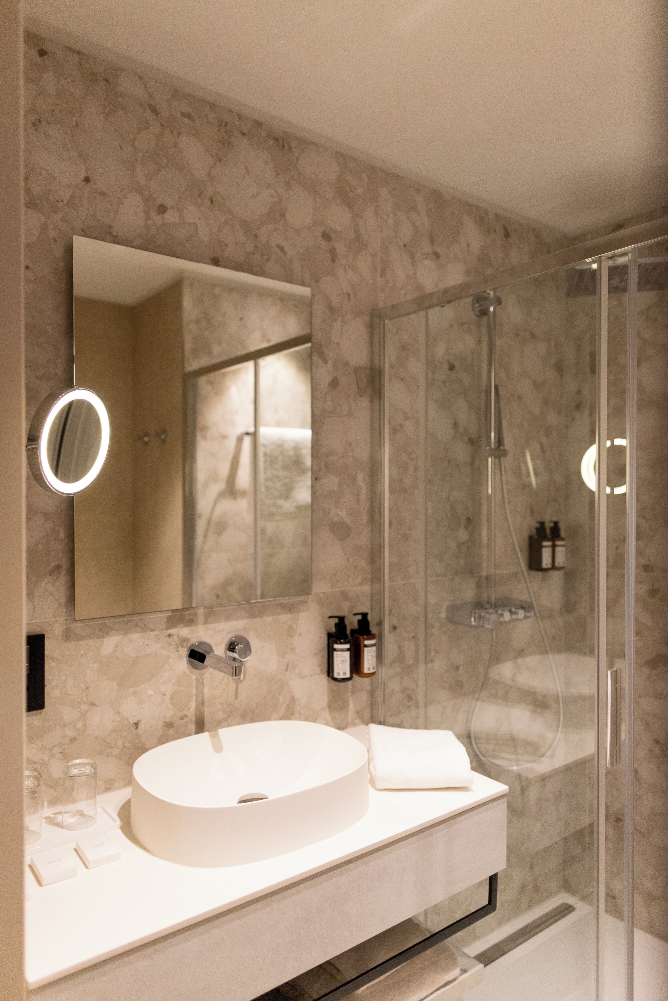 Un baño moderno con un lavabo redondo, un espejo grande y una ducha con cerramiento de vidrio.