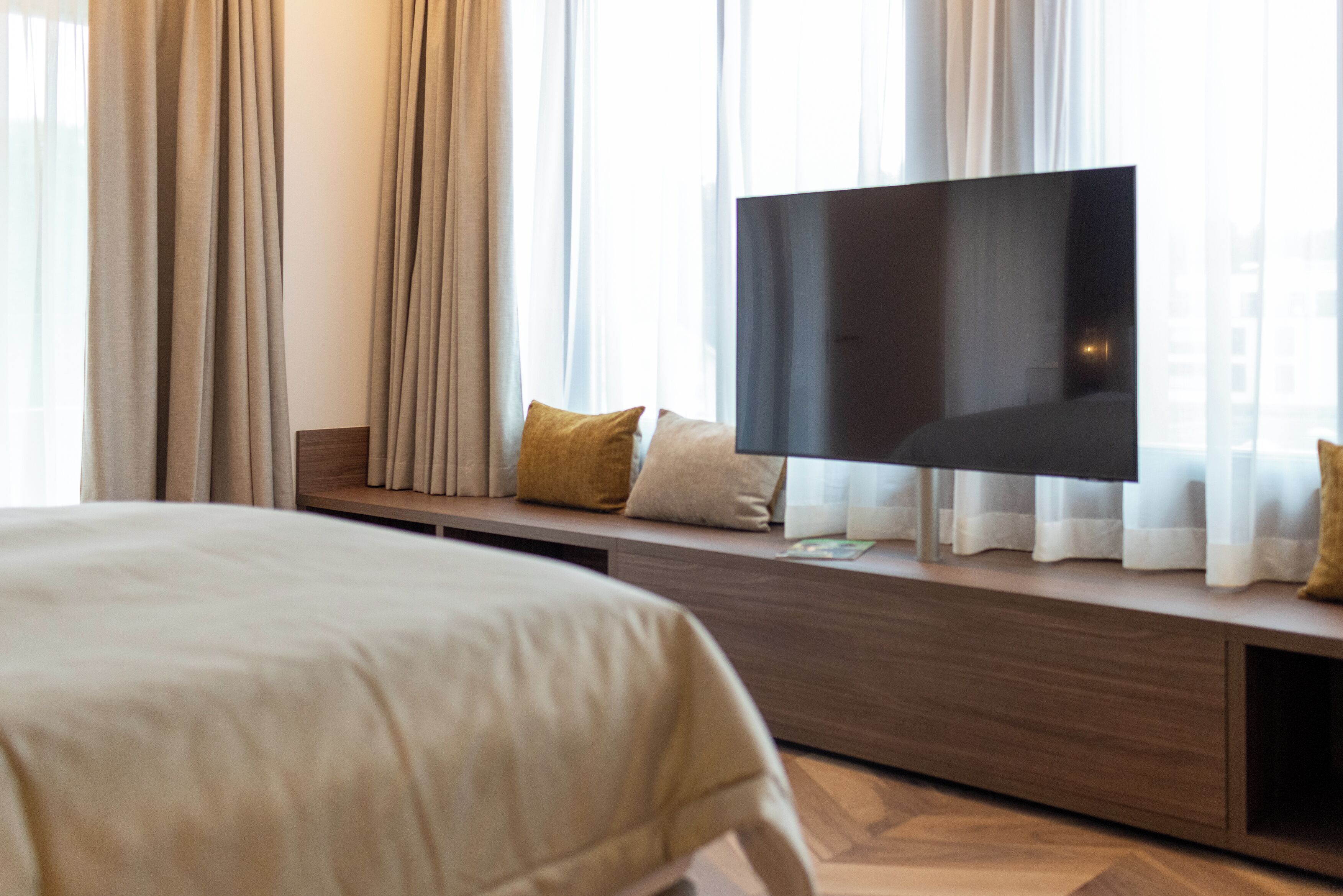 Une chambre d’hôtel avec un lit, un téléviseur posé sur une console en bois et des rideaux.