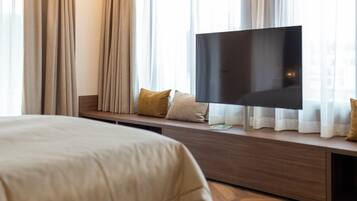 Une chambre d’hôtel avec un lit, un téléviseur posé sur une console en bois et des rideaux.