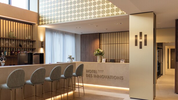 Un espace d’accueil moderne pour l’hôtel, comprenant un bar, des sièges et une enseigne indiquant « HÔTEL DES INNOVATIONS ».