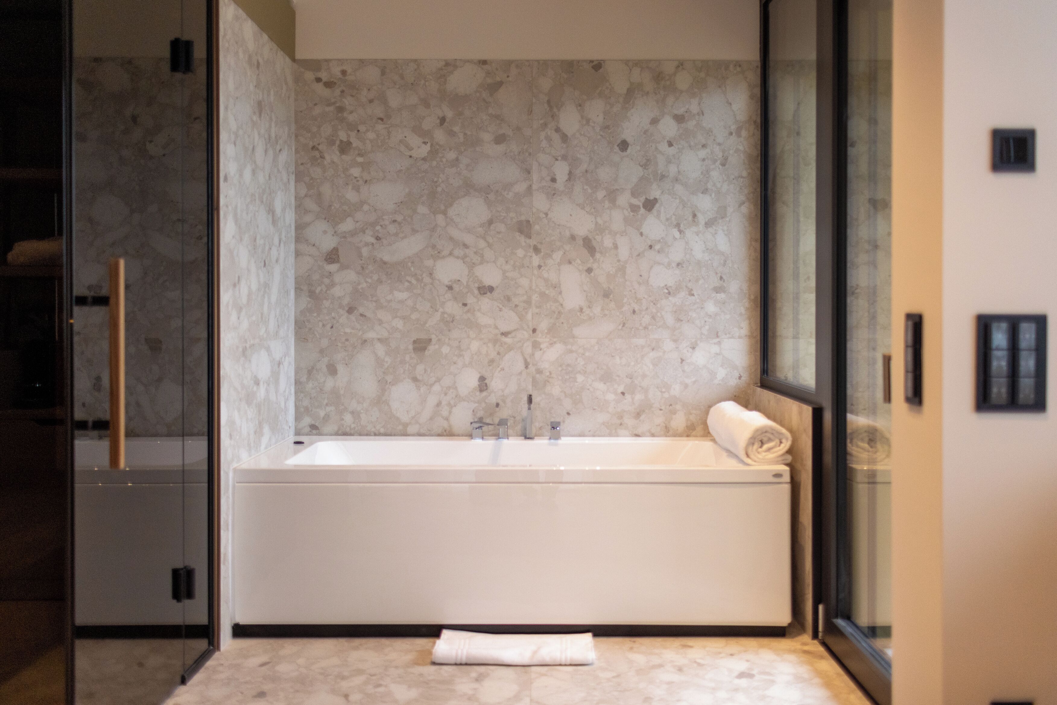 A modern bathroom with a freestanding bathtub, a glass shower enclosure, and a marble backsplash.