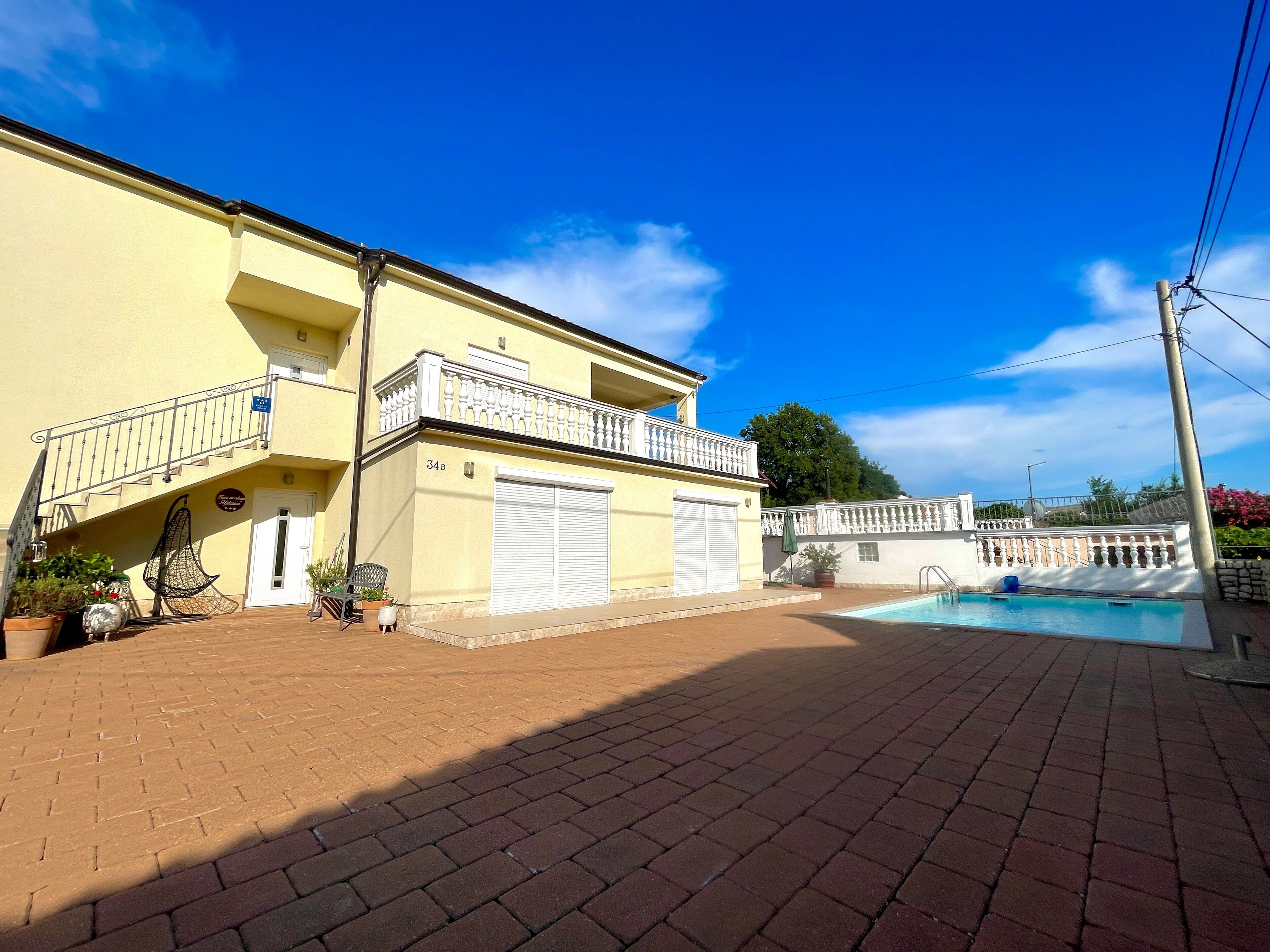 Un edificio de dos pisos con piscina, balcón y entrada pavimentada.