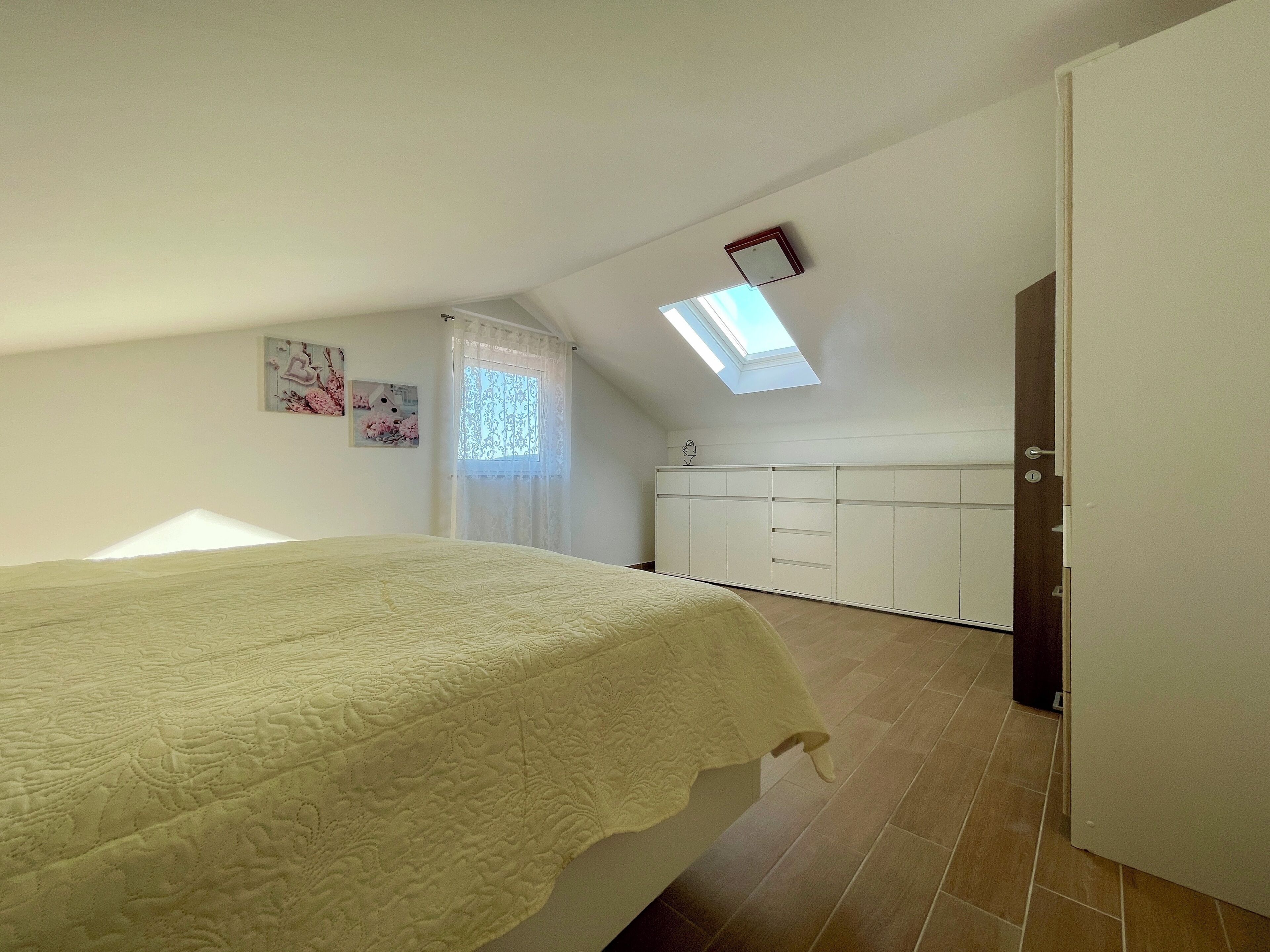 Un dormitorio con cama, armario, tragaluz y ventana con cortinas.
