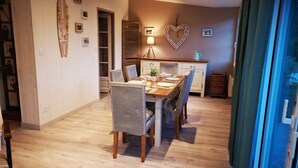 Un comedor con una mesa de madera y sillas de mimbre, una cocina al fondo y una decoración con forma de corazón en la pared.