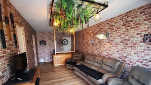 Un salón acogedor con pared de ladrillo, suelo de madera, un sofá, un televisor y plantas colgantes.