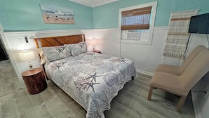 A bedroom with a bed, bedside table, lamp, chair, and a wall-mounted air conditioner.