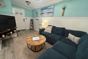 A living room with a television, a sofa, a coffee table, and a painting on the wall. - Auralee Unit 1 - Beach Access - Island Realty (Grand Isle)