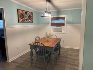 Un comedor con mesa y sillas de madera, una lámpara colgante y un adorno en la pared.