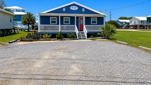A two-story building with a blue exterior and a red door, featuring a small porch and a staircase leading to the entrance. - Auralee Unit 1 - Beach Access - Island Realty (Grand Isle)