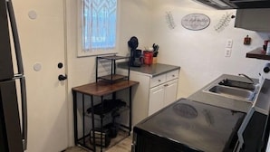 A compact kitchen with a refrigerator, a sink, a countertop, and a window with patterned curtains. - Auralee Unit 1 - Beach Access - Island Realty (Grand Isle)