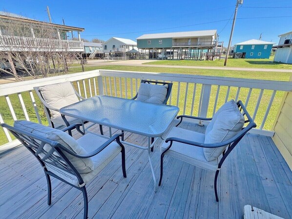 A deck with a glass-top table and four chairs, surrounded by a white railing.