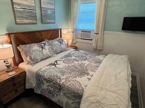 A bedroom with a bed, nightstand, lamp, air conditioning unit, and artwork on the wall. - Auralee Unit 2 - Beach Access - Island Realty (Grand Isle)