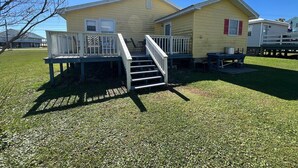 A two-story yellow mobile home with a white exterior, a front porch, and a staircase leading to the entrance. - Auralee Unit 2 - Beach Access - Island Realty (Grand Isle)