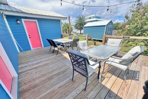 A wooden deck with outdoor furniture, a blue shed, and a red door.