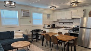 A modern kitchen with white cabinets, a stainless steel refrigerator, and a dining area with a wooden table and chairs. - Auralee Unit 2 - Beach Access - Island Realty (Grand Isle)