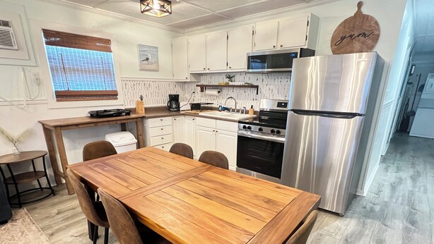 A compact kitchen with white cabinets, a stainless steel refrigerator, a microwave, and a wooden dining table with chairs. - Auralee Unit 2 - Beach Access - Island Realty (Grand Isle)