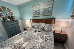 A bedroom with a bed, a dresser, a nightstand, a lamp, a mirror, and two wall-mounted paintings.