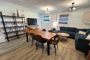 A modern living room with a wooden dining table, a sofa, and a television. - Auralee Unit 2 - Beach Access - Island Realty (Grand Isle)