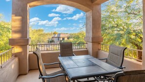 Un balcon extérieur avec une table et des chaises, donnant sur des arbres et un bâtiment en arrière-plan.