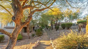 Un chemin bordé d’arbres et d’arbustes, qui mène à un bâtiment au design moderne.