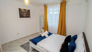 Een slaapkamer met een bed, een schilderij aan de muur, een raam met gordijnen en een lamp.