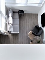 Una sala de estar moderna con un sofá seccional gris, una mesa de centro redonda negra, un sillón beige y una pequeña mesa redonda con una planta.