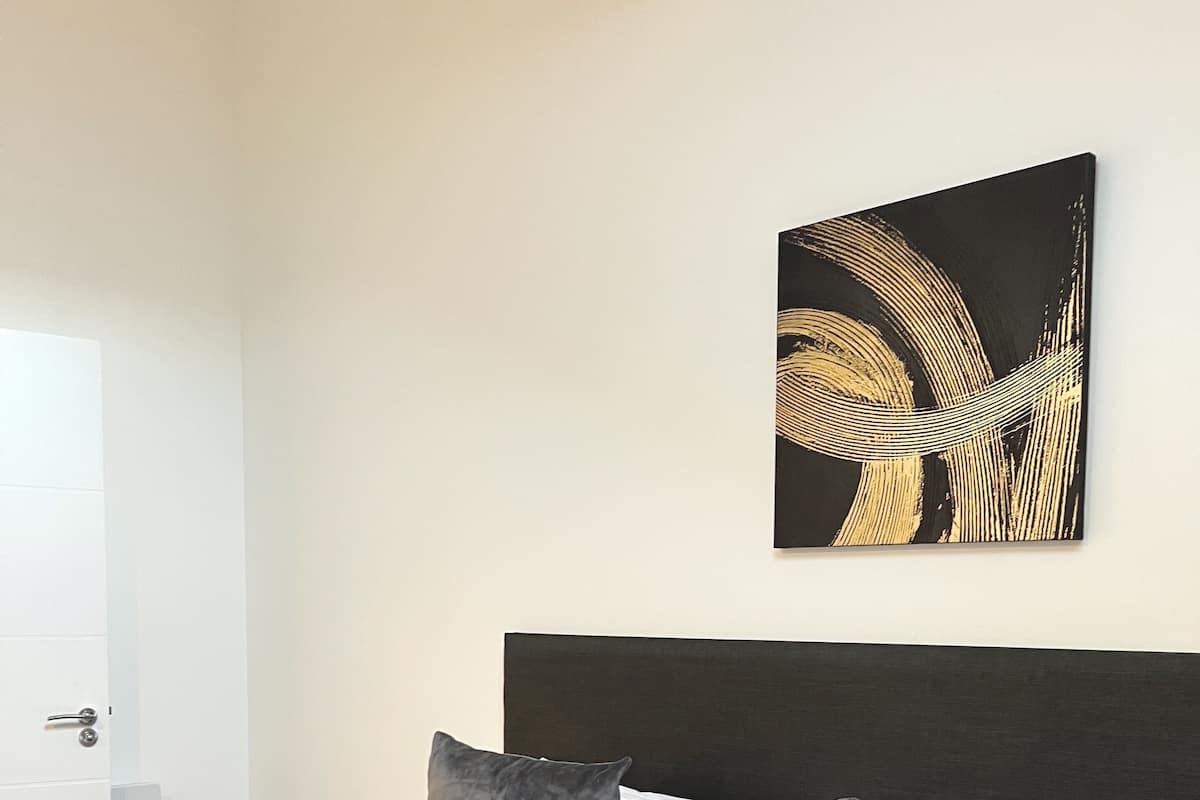 Una camera d'albergo moderna con un letto rifatto, un grande quadro astratto sulla parete e vista sulla città attraverso la finestra.