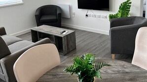 Un soggiorno moderno con una TV a schermo piatto montata a parete, un tavolino da caffè e due divani.