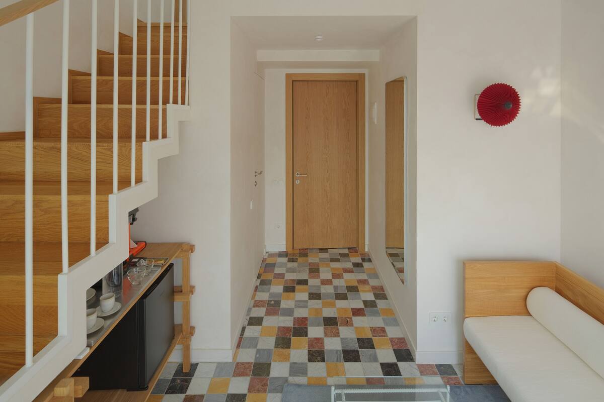 A two-story apartment with a staircase, a small kitchen area, a sofa, and a patterned floor.