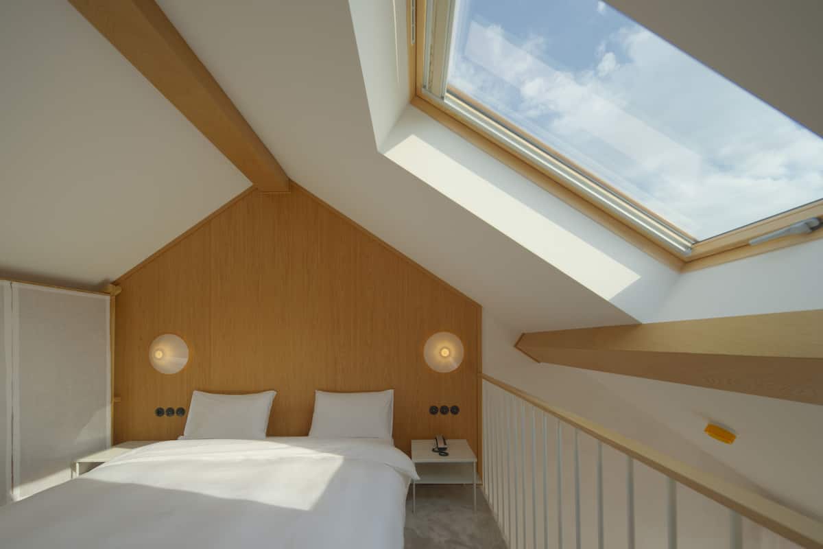 A bedroom with a skylight, a bed, bedside tables, and a nightstand.