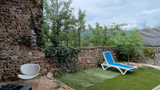 Un mur de pierres avec une chaise blanche et un fauteuil bleu dans un coin du jardin.