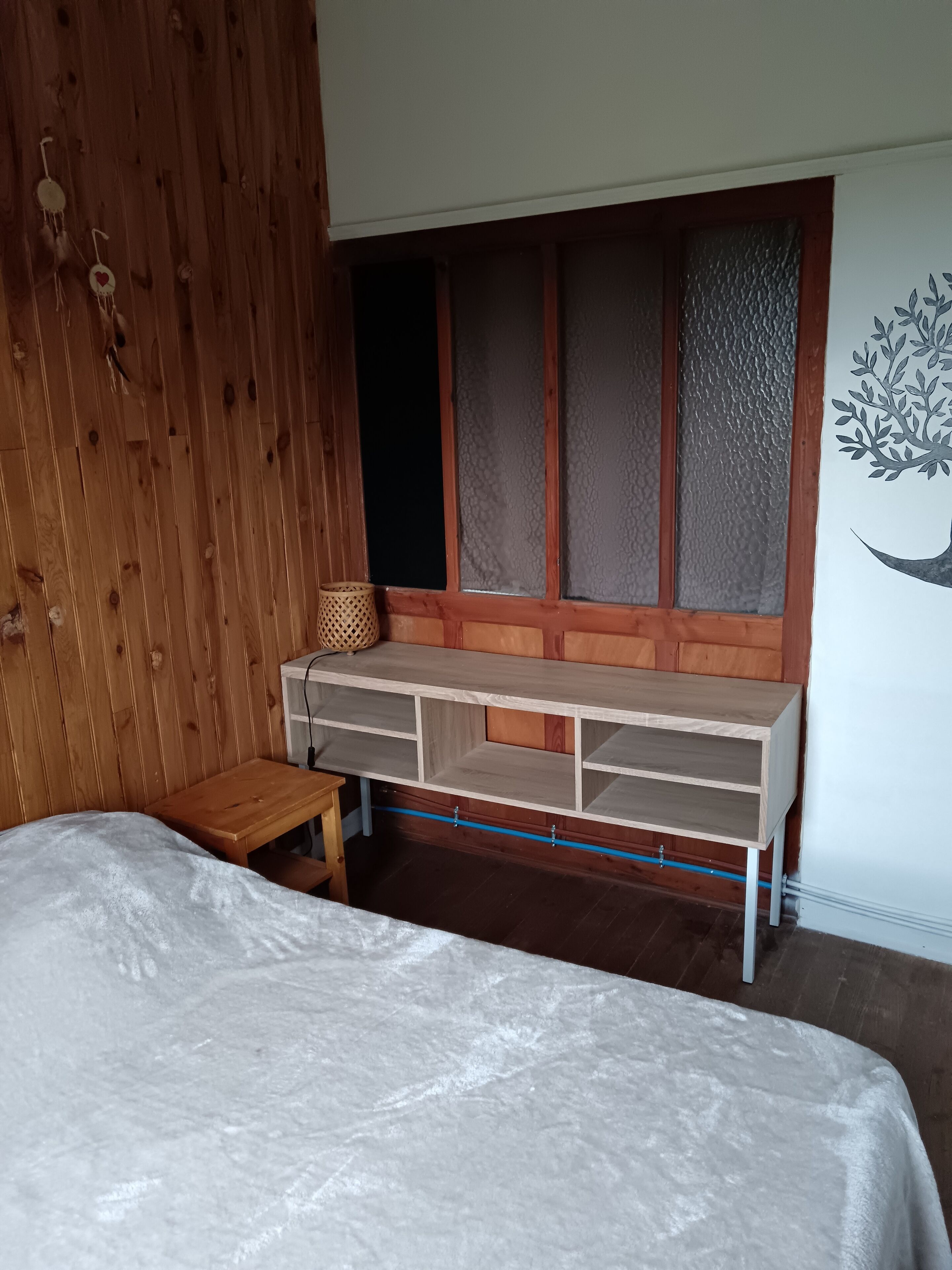 Une chambre à coucher avec un lit, un bureau en bois et une fenêtre dont les vitres sont en verre dépoli.