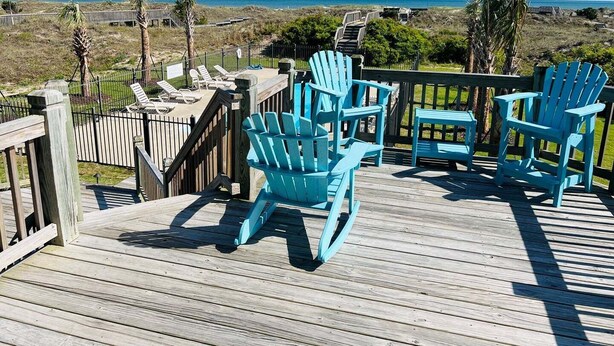 Une terrasse en bois avec des fauteuils Adirondack turquoise et une vue sur l’océan.
