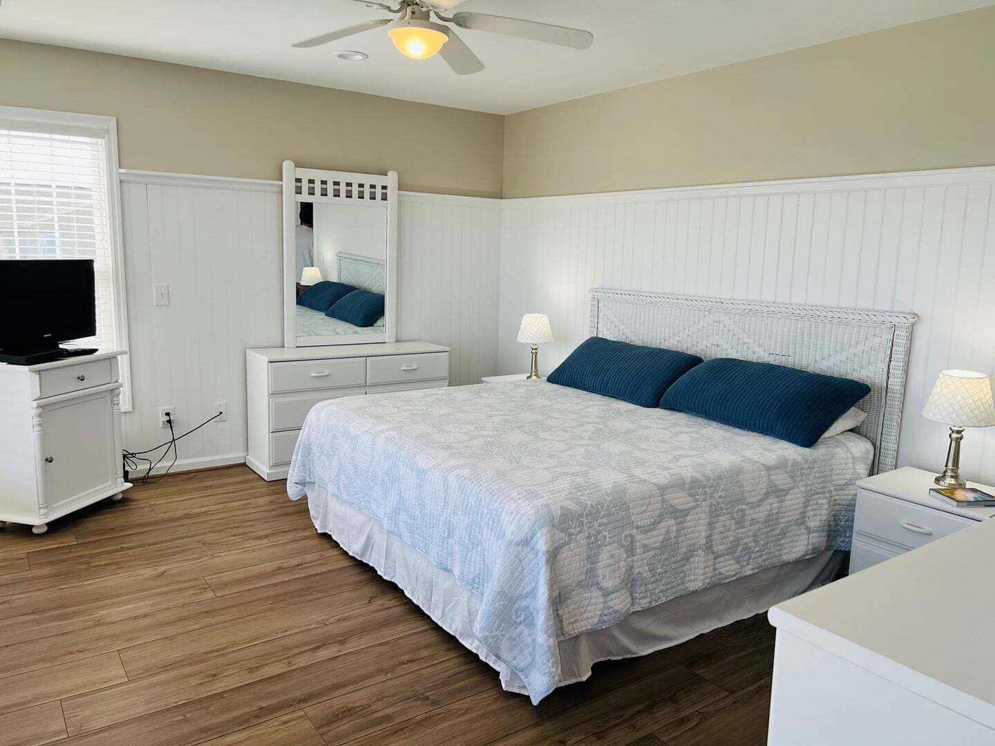 A bedroom with a bed, a dresser, a television, a ceiling fan, and a mirror.