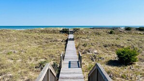 Une promenade en bois qui mène à une plage bordée de dunes, sous un ciel dégagé.