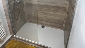 A walk-in shower with a glass door, a showerhead, and a control panel.