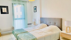 A double bed with a grey headboard, two bedside tables with lamps, a window with a curtain, and a wall-mounted picture frame.