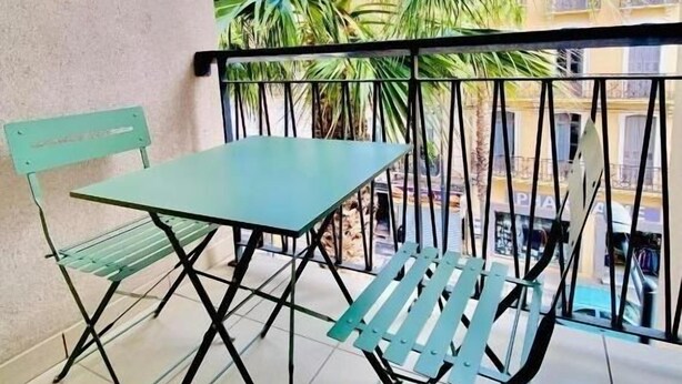 A balcony with a table and chairs, overlooking a building and palm trees.
