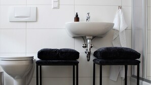A modern bathroom with a white sink, two black stools, a toilet, and a mirror above the sink. - Piesteritzer Hof - Hotel Garni (Lutherstadt Wittenberg)