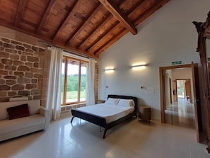 A bedroom with a stone wall, a bed, a sofa, a window with curtains, and a wooden ceiling. - New apartment with garden in a rural house with sea views (Vizcaya)
