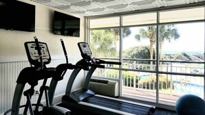 A gym with treadmills and exercise equipment, large windows with a view of a pool and palm trees.