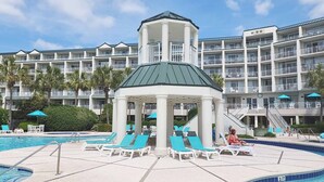 A hotel with a swimming pool, lounge chairs, and a gazebo structure.