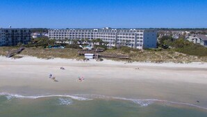 A beachfront hotel with multiple floors, a sandy beach, and a clear sky.