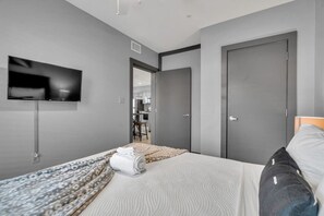 Una habitación de hotel moderna con una cama, un televisor montado en la pared y una puerta que da a un baño.