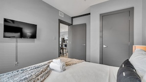Una habitación de hotel moderna con una cama, un televisor montado en la pared y una puerta que da a un baño.