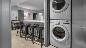 Un lavadero moderno con dos lavadoras apiladas, una zona de bar con taburetes y una puerta que da a otra habitación.