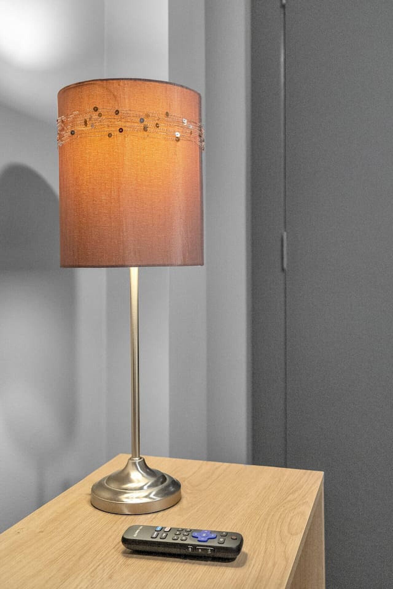 Eine stehende Lampe mit zylindrischem Lampenschirm auf einem Nachttisch neben einer Fernbedienung.