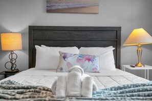 Un lit bien fait, avec des draps blancs, un coussin décoratif et une serviette pliée posée sur le lit.